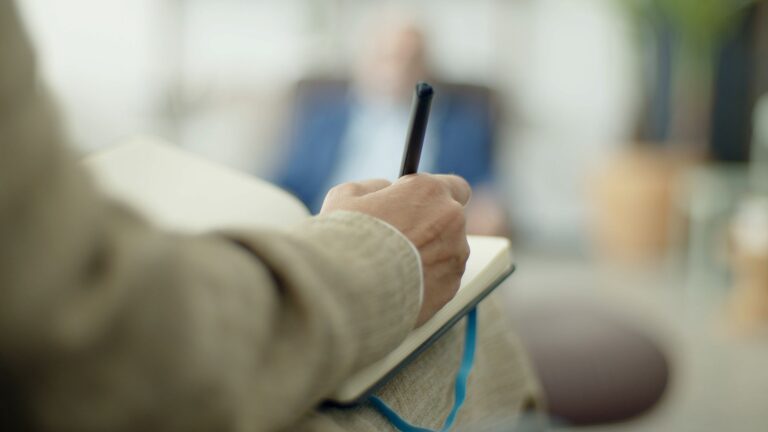 Close-up of an adult writing in a notebook with a pen, depth of field effect.