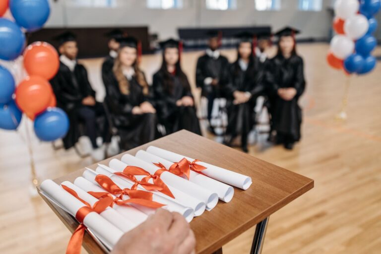 Graduation ceremony with students seated, diplomas, and festive balloons.