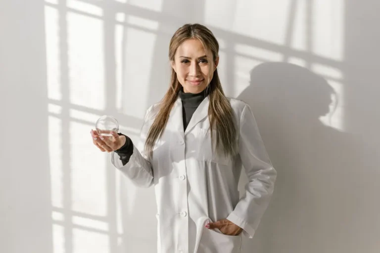 Asian acupuncturist holding a ventosa glass cup, smiling in a white coat, indoors.