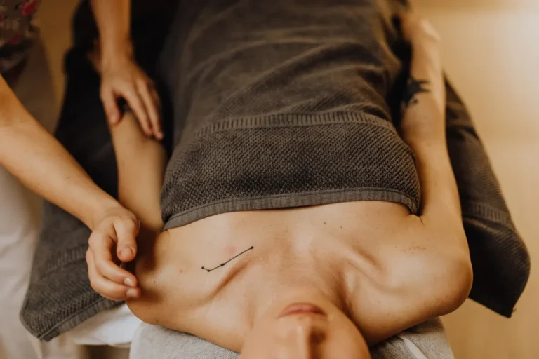 A calming massage therapy session with a tattooed woman covered in a towel, focused on relaxation and wellness.
