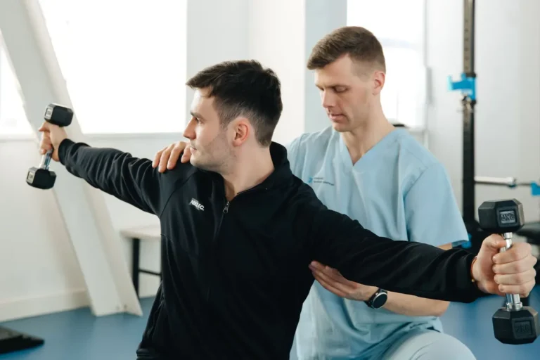 A physiotherapist assists a patient lifting dumbbells during a therapy session in a clinic.