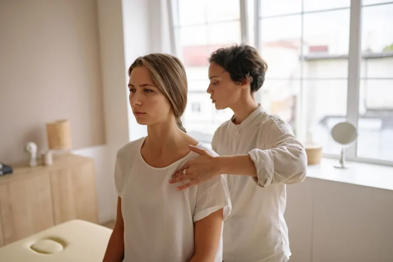 A woman receives shoulder therapy from a therapist in a serene room with natural light.